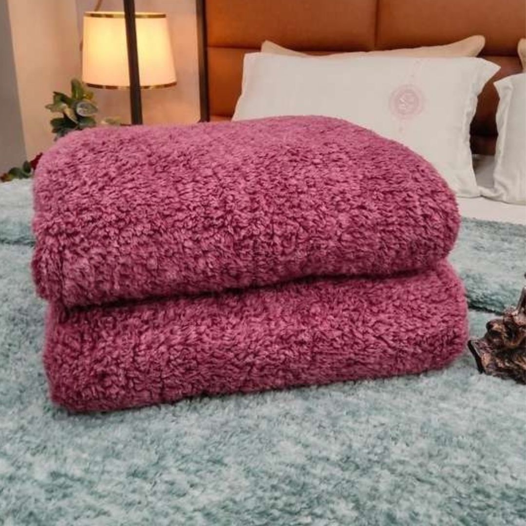 Folded pink blanket on a bed with a lamp and pillows in the background