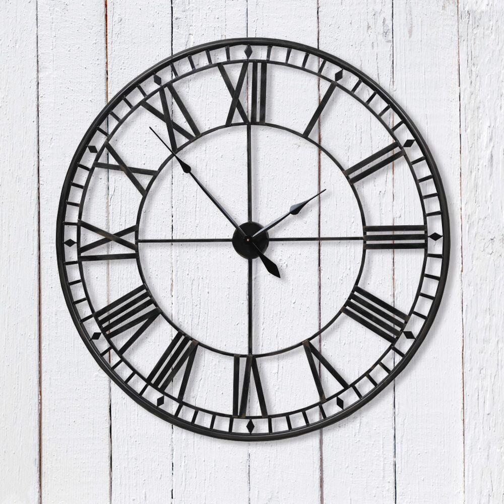 Large black wall clock with Roman numerals on a white wooden background