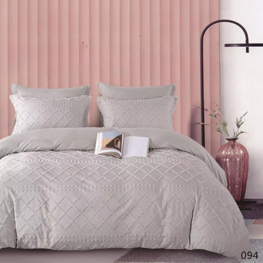 Gray quilted comforter set on a bed with a pink wall and decorative elements.
