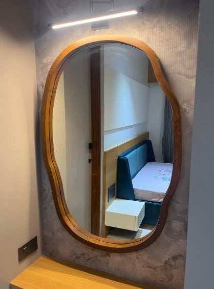 Wooden-framed oval mirror on a textured wall with a reflection of a room.