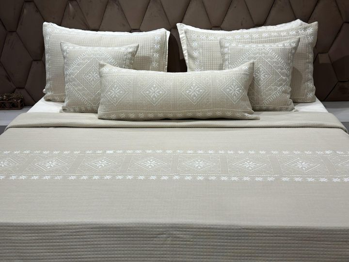 Neatly arranged bed with patterned bedding and pillows against a textured headboard.