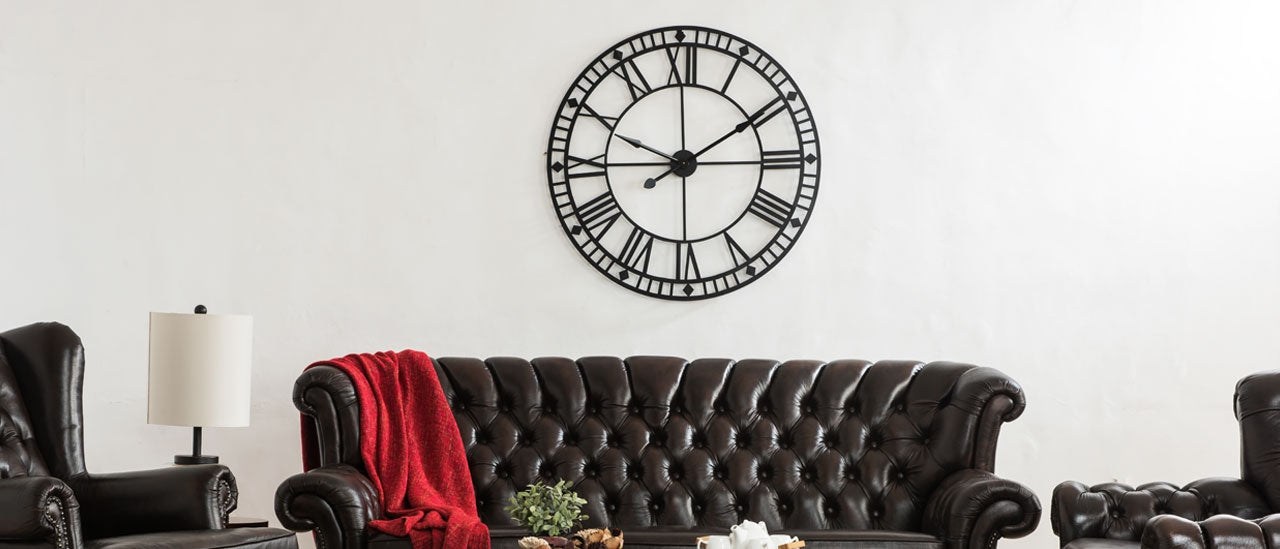 Black leather sofa with a red blanket, black armchair, and decorative clock on a white wall.
