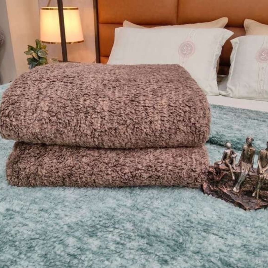 Stack of brown textured blankets on a bed with decorative elements.