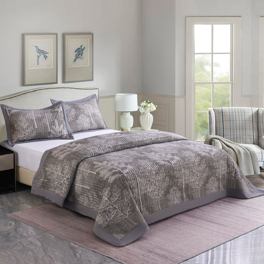Bedroom with gray patterned bedding, pillows, and a lamp.