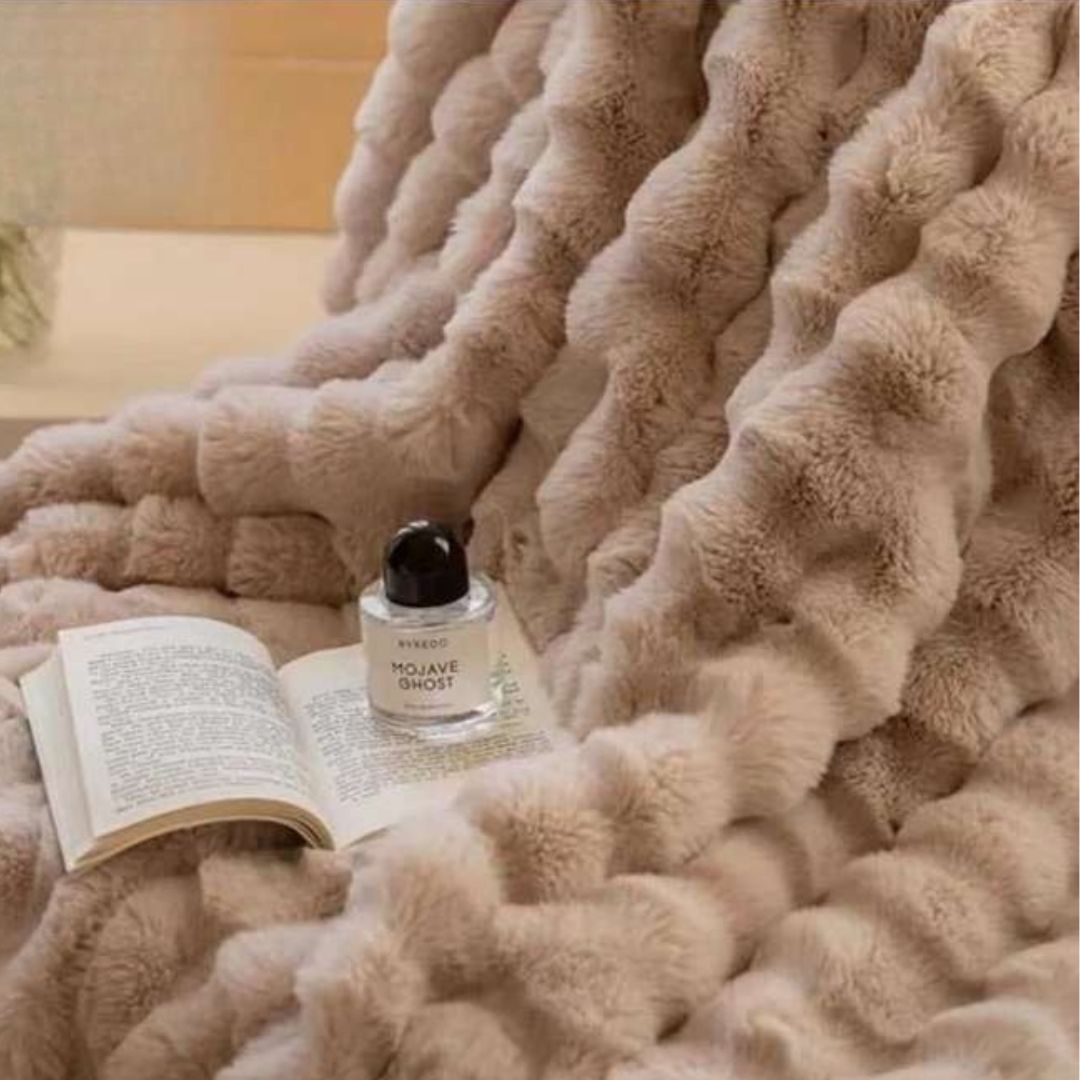 Beige fluffy blanket with an open book and a bottle of Mojave Duet on a soft surface.