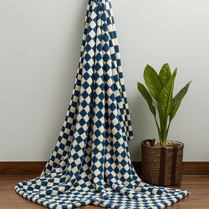 Blue and white checkered blanket draped over a chair next to a potted plant on a wooden floor.