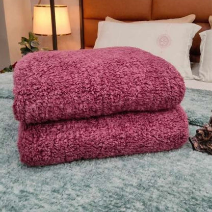 Folded pink blanket on a bed with a lamp and pillows in the background