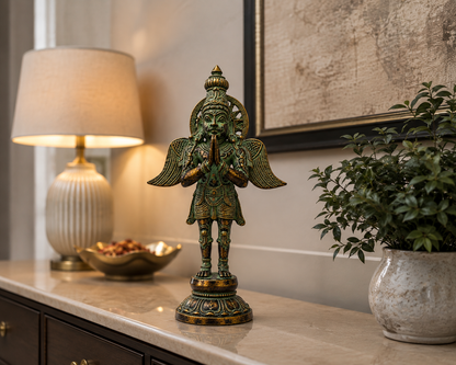 An ornate bronze statue of a winged deity with a green patina finish and gold accents, displayed on a marble console table in a beautifully decorated room next to a lit lamp and a potted plant.