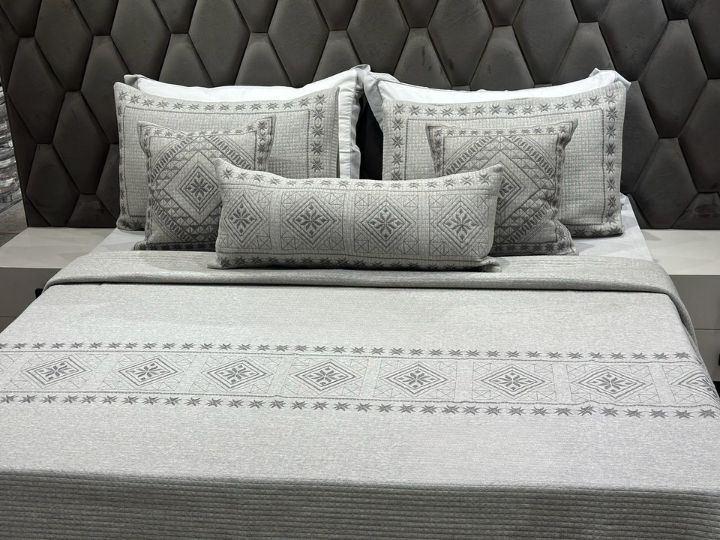 Gray patterned bedding set on a bed with a tufted headboard.