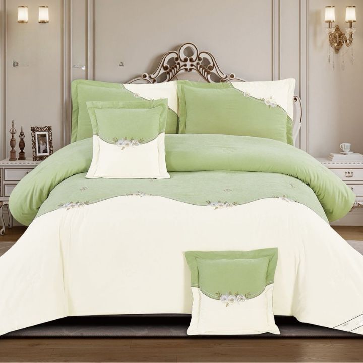 Green and white bedding set on a bed with decorative pillows and a headboard.