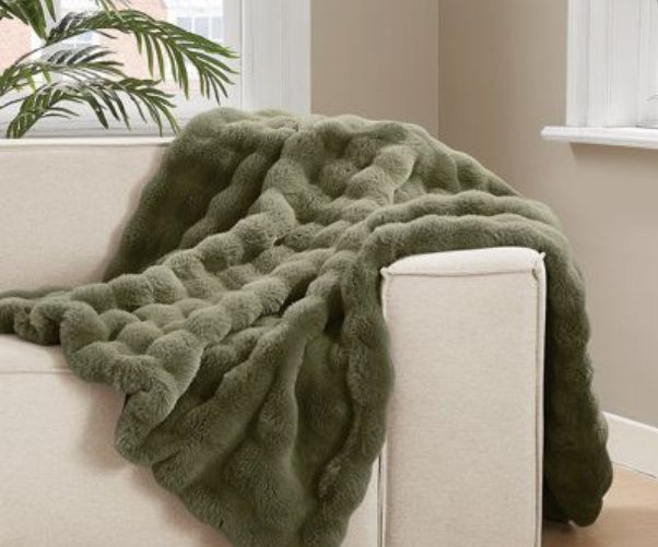 Green blanket draped over a beige sofa with a neutral background
