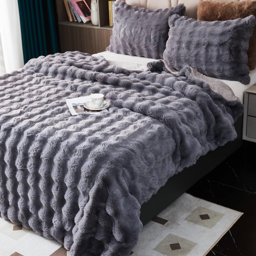 Gray textured blanket on a bed with pillows and a small table.