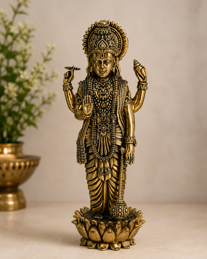 A brass Lord Hanuman statue standing on a lotus base, photographed on a light beige surface with a softly blurred neutral background and a decorative plant pot at the side.