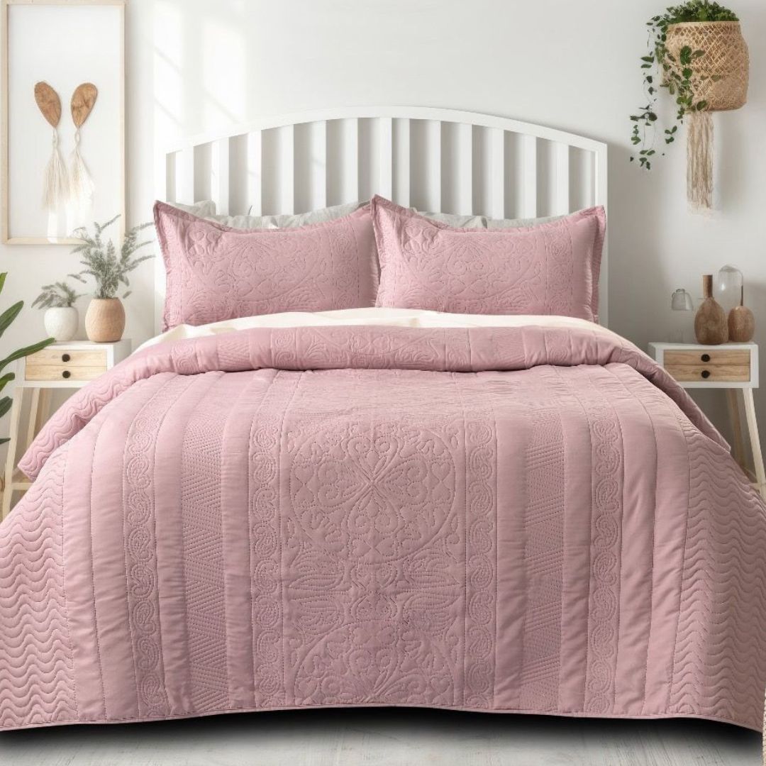Pink quilt set on a bed in a bedroom with white walls and decor.