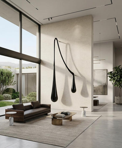 A modern living room interior with a sculptural black wall-mounted light fixture shaped like two elongated teardrop forms, above a low brown sofa and wood coffee table on a large beige rug.