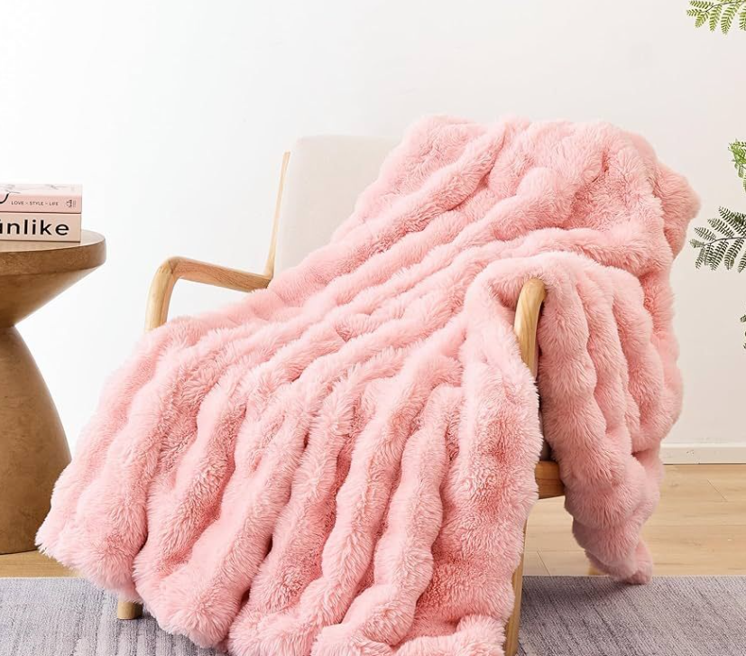 Pink fluffy blanket draped over a chair in a room with a table and books.
