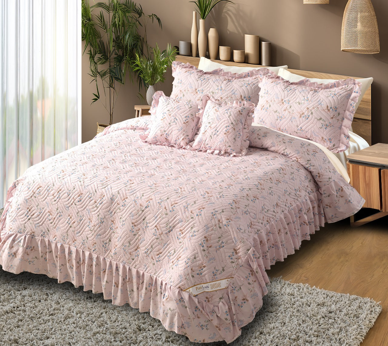 Pink floral bedspread set on a bed in a bedroom with plants and decor.