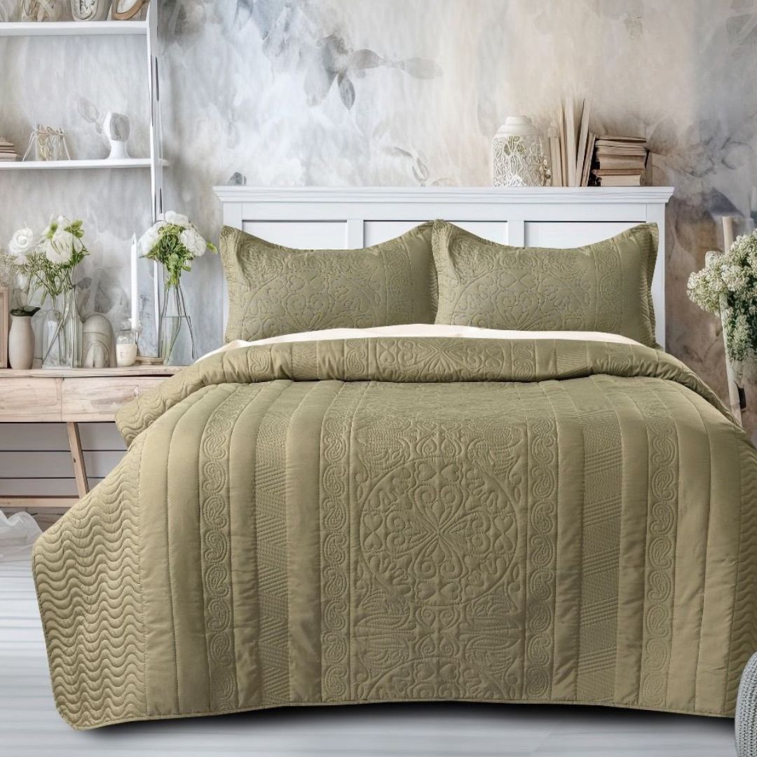 Green quilted coverlet set on a bed in a bedroom setting with a desk and decorative items.