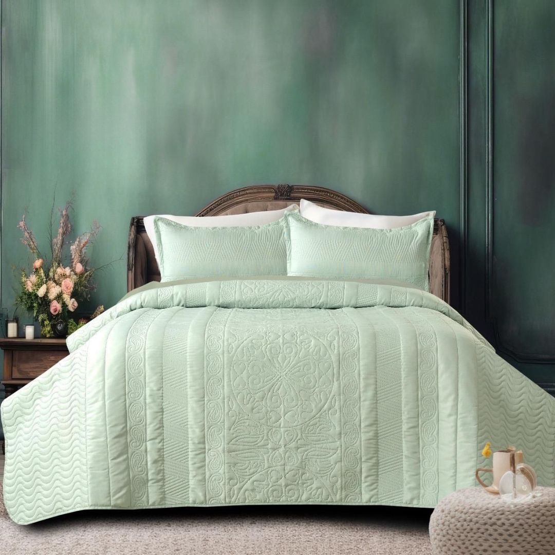 Green quilted bedspread on a bed with matching pillows against a green wall.