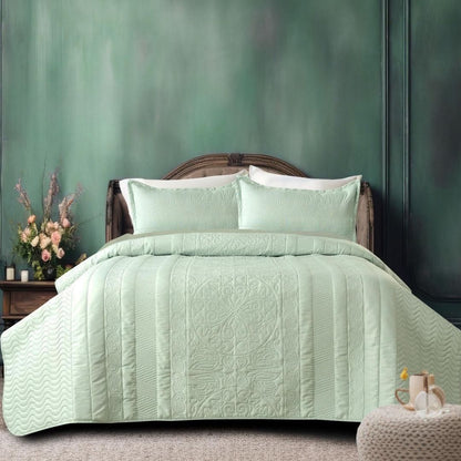Green quilted bedspread on a bed with matching pillows against a green wall.