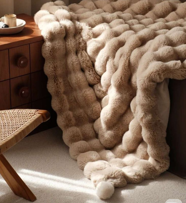 Beige textured blanket draped over a chair in a cozy room with wooden furniture.