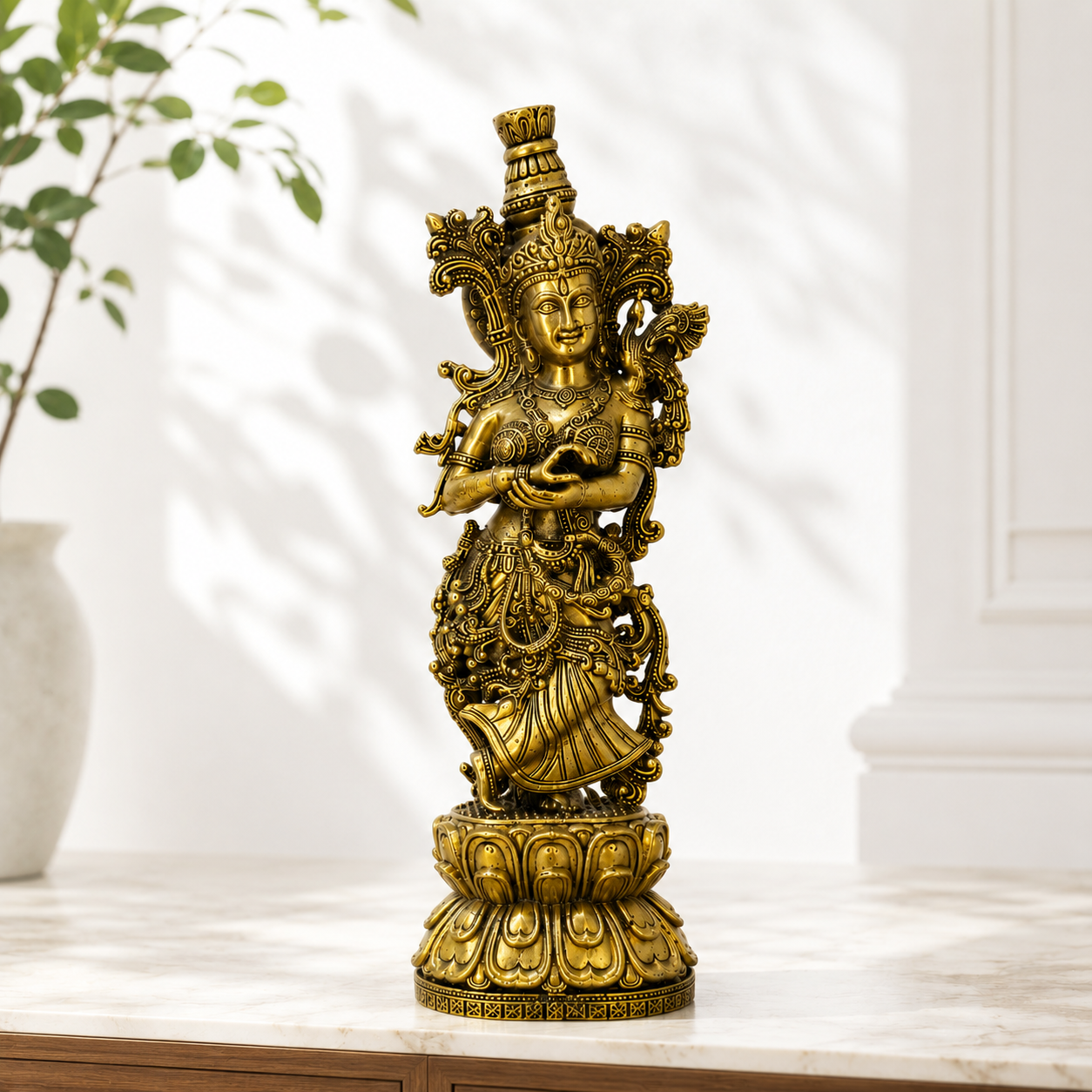 A golden brass statue of a Hindu goddess standing on a lotus pedestal, displayed on a marble tabletop with a blurred background of a plant and wall shadows.