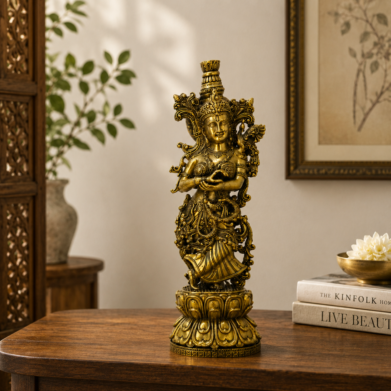 An ornate golden statue of a Hindu deity standing on a lotus pedestal, displayed on a wooden table in a styled room setting with books and a framed print in the background.