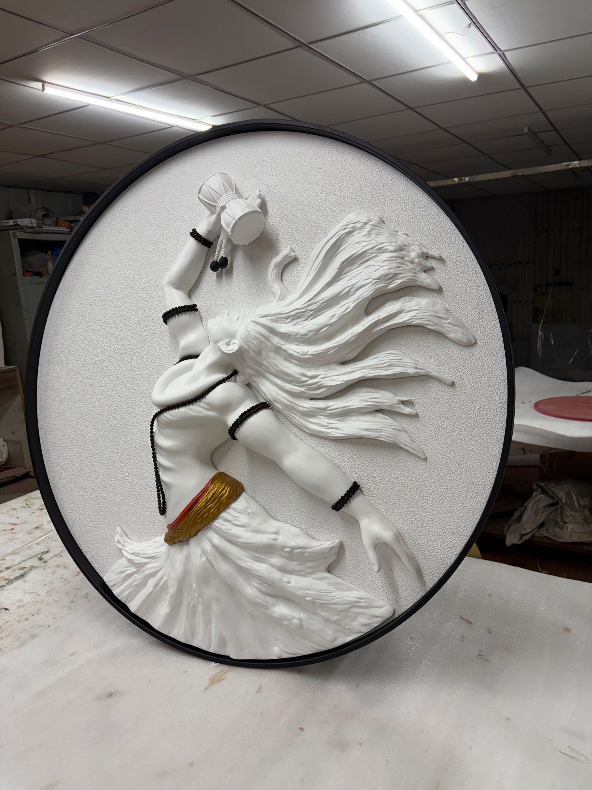 Round white sculpture of a person with long hair on a black base, in an indoor setting.