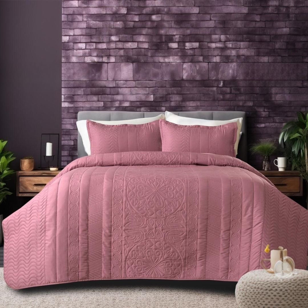 Pink quilted coverlet on a bed with matching pillows against a purple brick wall.
