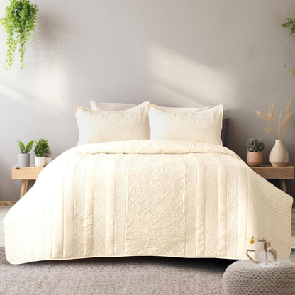 Beige quilted coverlet on a bed with pillows in a bedroom setting.
