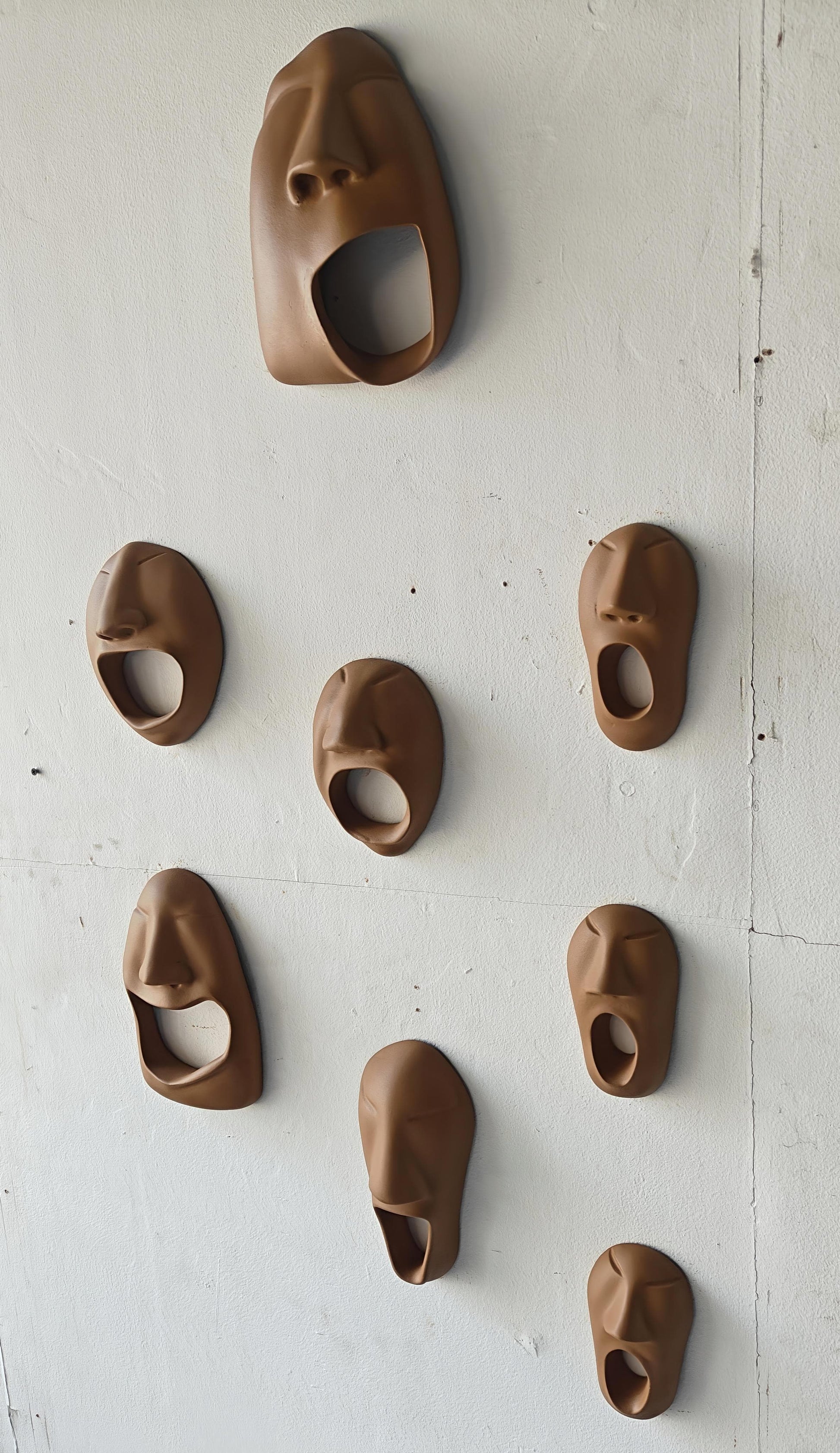 Set of brown ceramic face-shaped wall hooks on a white wall.