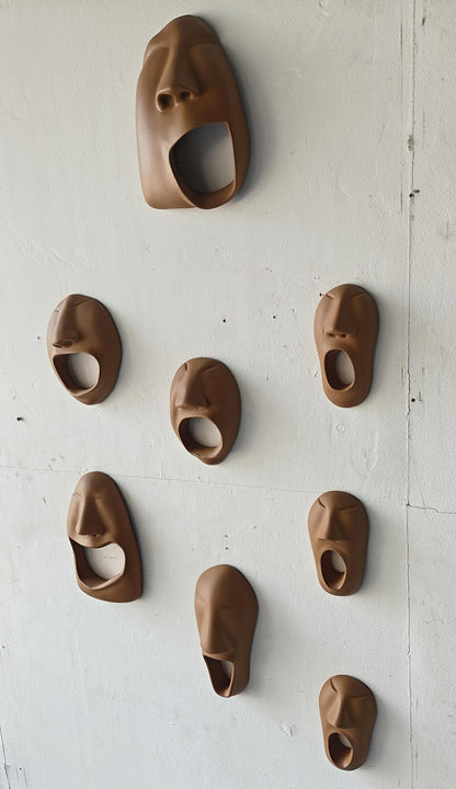 Set of brown ceramic face-shaped wall hooks on a white wall.