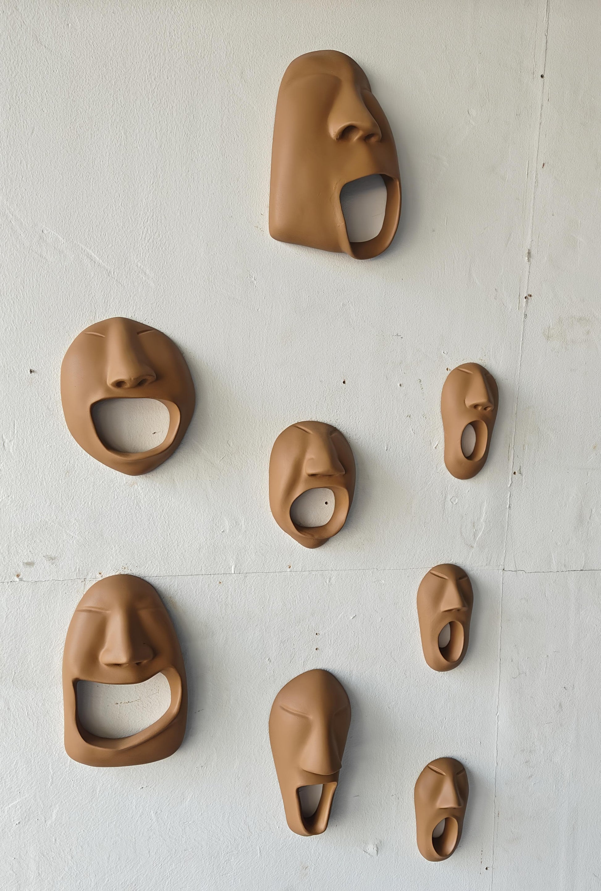Set of brown ceramic face-shaped bottle openers on a white wall.