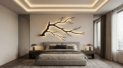 A modern bedroom featuring a large black branch wall art piece with warm LED backlighting mounted above a bed with neutral-toned bedding.