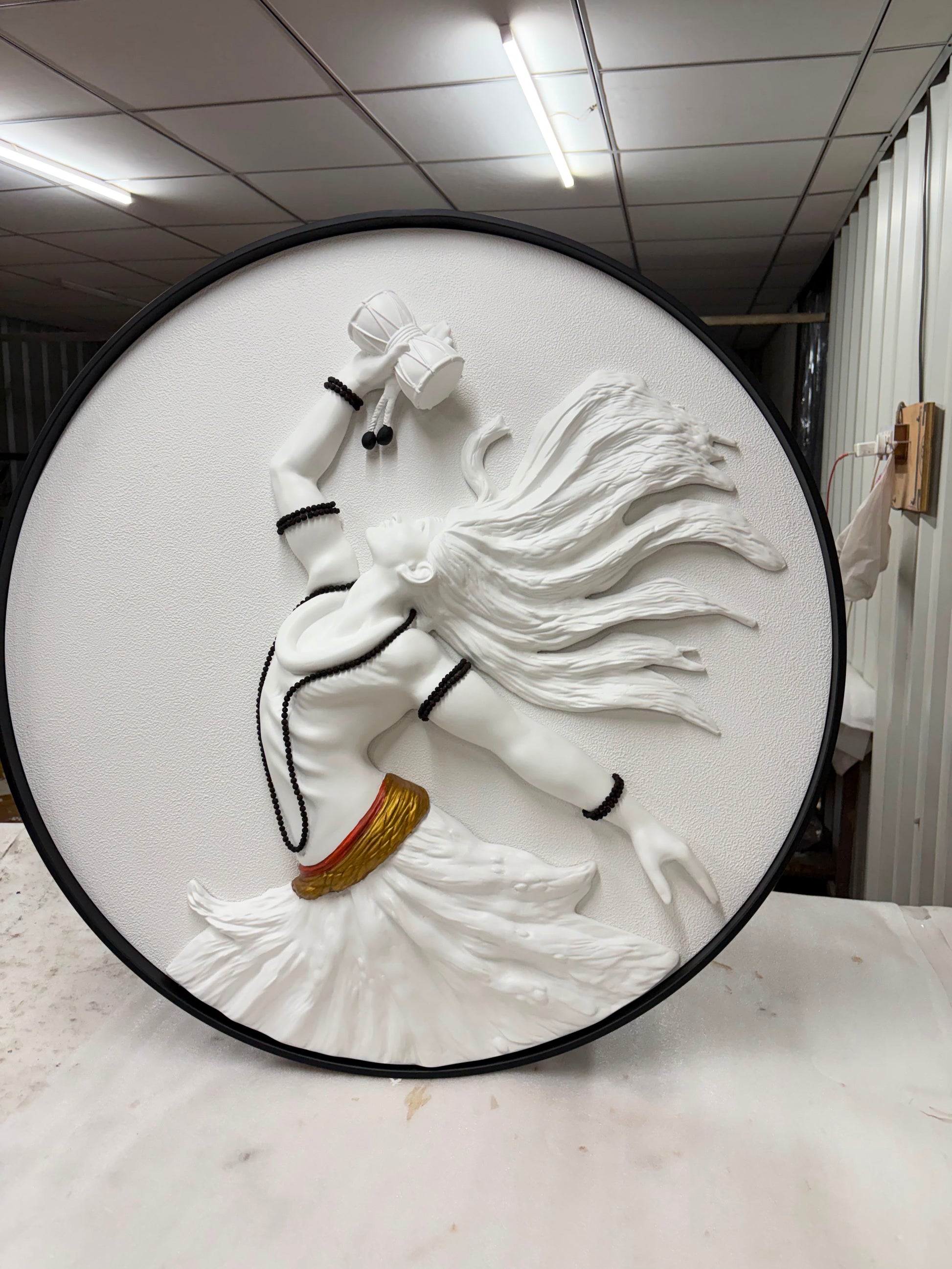 White relief sculpture of a figure with a long hair on a circular black frame.