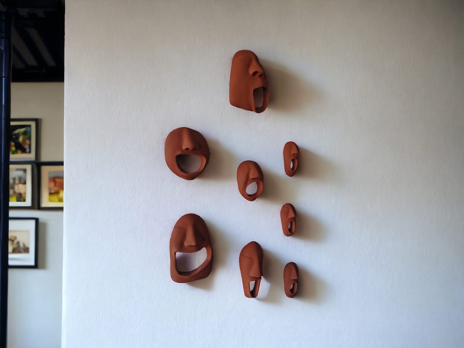 Set of terracotta bottle openers shaped like faces on a white wall.