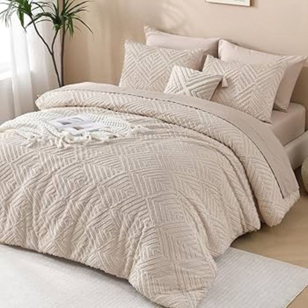 Beige textured comforter set on a bed with pillows and a plant in the background.