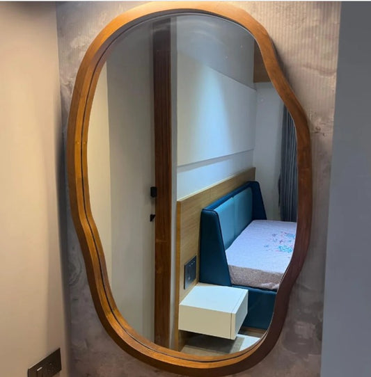 Oval mirror with wooden frame reflecting a bedroom with blue bed and white nightstand.