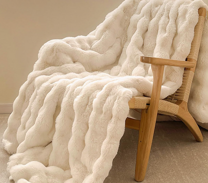 White fluffy blanket draped over a wooden chair against a beige wall.