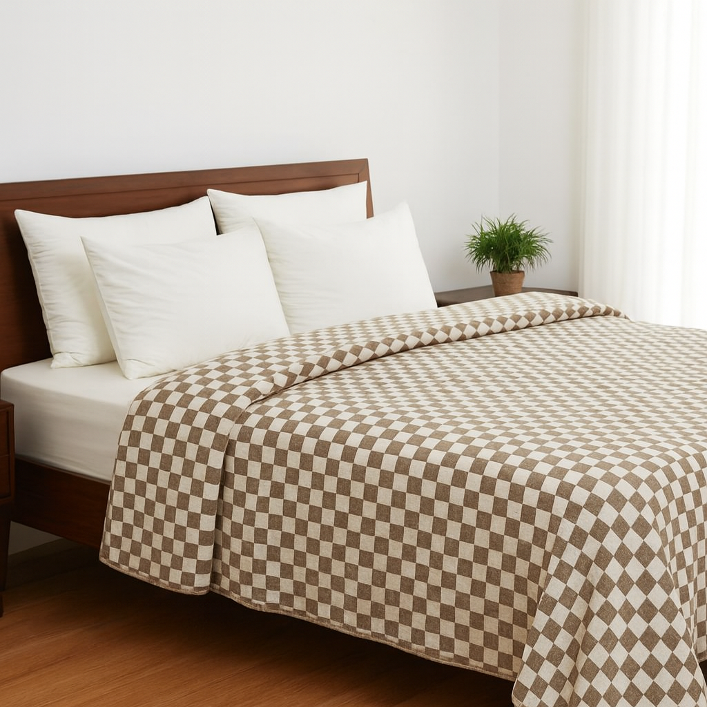 Bed with checkered brown and beige duvet and white pillows in a room with a plant.