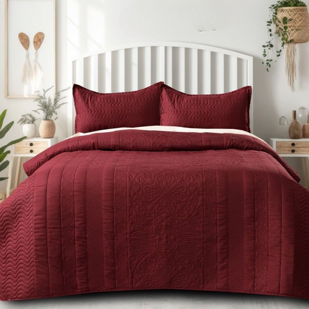 Red quilt set on a bed in a bedroom with white walls and decor.