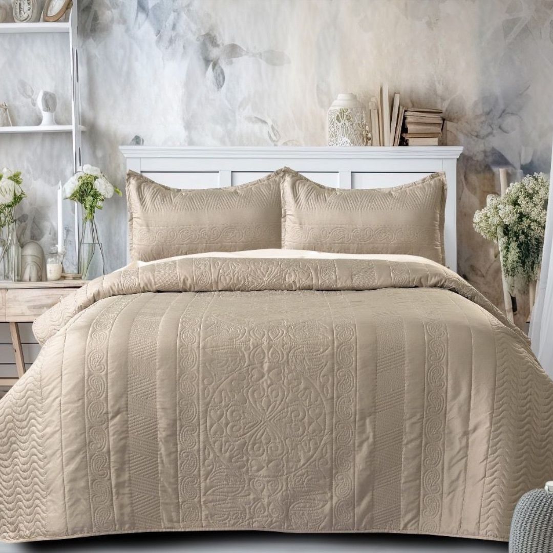 Beige quilted comforter set on a bed with decorative pillows in a bedroom setting.