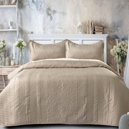 Beige quilted comforter set on a bed with decorative pillows in a bedroom setting.