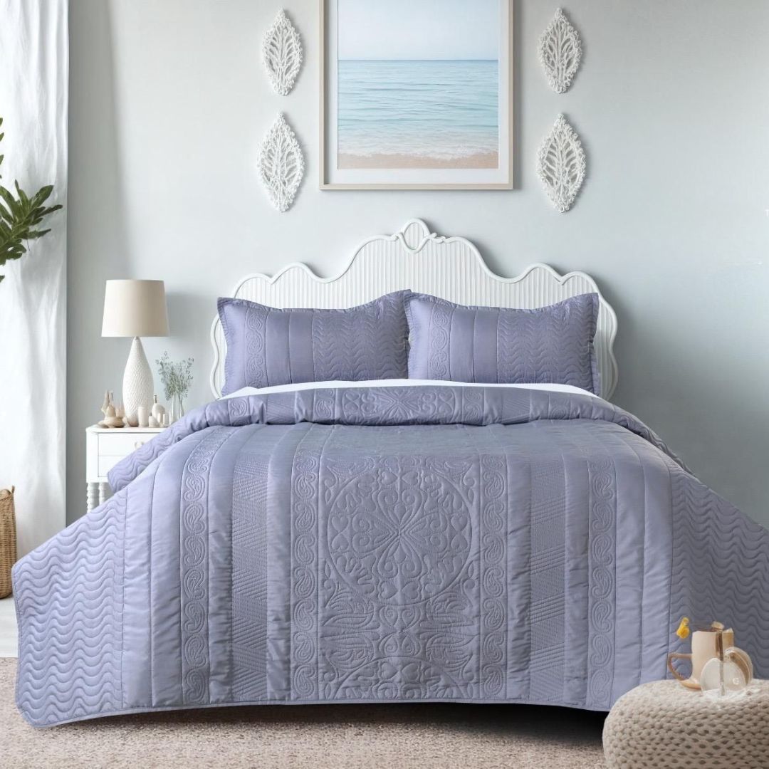 Bedroom with a bed covered in purple quilt and pillows, decorated with a lamp and artwork on the wall.