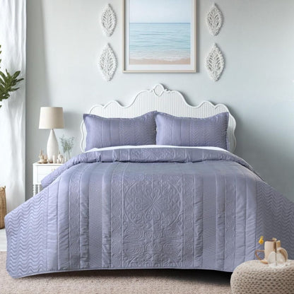 Bedroom with a bed covered in purple quilt and pillows, decorated with a lamp and artwork on the wall.