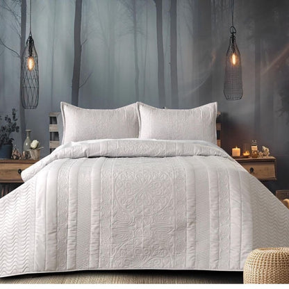 Quilted bedspread on a bed with a forest-themed wall in the background