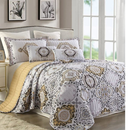 Decorative quilt set with geometric patterns on a bed in a well-lit room.