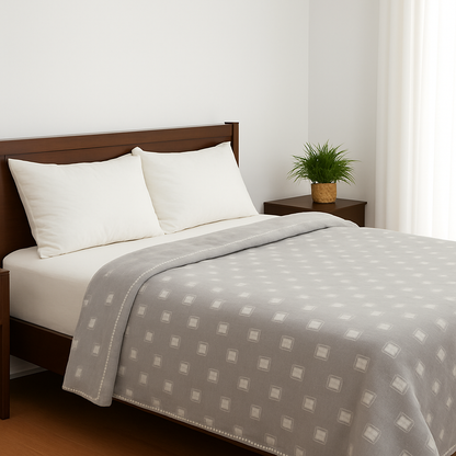 Bed with gray patterned blanket and white pillows in a room with a plant and nightstand.