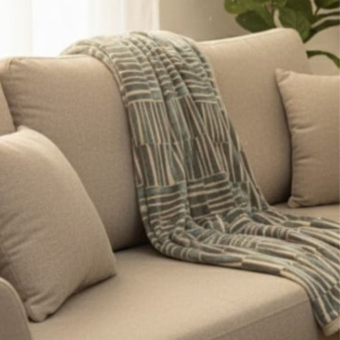 Beige sofa with a plaid blanket draped over it in a living room setting.