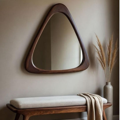 Triangular wooden mirror on a beige wall with a bench and decorative vase below.